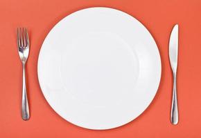 top view of porcelain plate, fork, knife on red photo