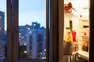 Open door of refrigerator with meal in evening photo