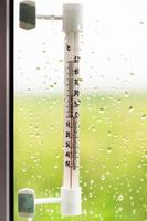 thermometer and rain drops on window glass photo