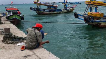 Lampung, September 10, 2022 A fisherman sticks his thread into the sea on the edge of small port looking for small fish and he very enjoying the moment. photo