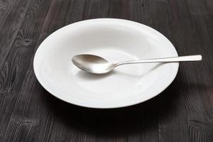 white deep plate with spoon on dark brown table photo