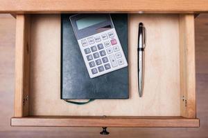 ballpen, calculator and notebook in open drawer photo