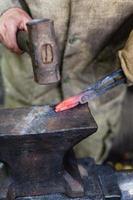 Blacksmith forges tongs with hammer on anvil photo