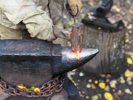 Blacksmith processing red hot iron rod on anvil photo