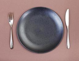 top view of black plate, fork, knife set on brown photo