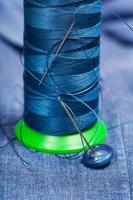 thread bobbin with needles, button on blue textile photo