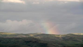 8k Regenbogen über grünen Hügeln mit spärlichen Bäumen video