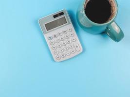 plano de calculadora azul y taza azul de café negro sobre fondo azul con espacio de copia. foto