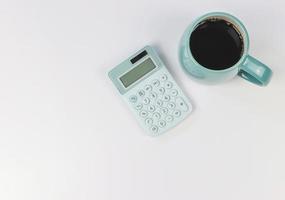 plano de calculadora azul y taza azul de café negro sobre fondo blanco con espacio de copia. foto