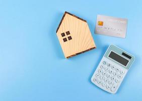 diseño plano de modelo de casa de madera, calculadora azul y tarjeta de crédito sobre fondo azul con espacio de copia. concepto de compra de vivienda. foto