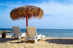 Empty sandy beach with parasol and two sunbeds against clear blue sea photo