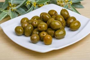 Green olives on the plate and wooden background photo