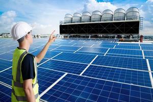 ingeniero eléctrico o mecánico profesional asiático, joven adulto que trabaja en la estación de energía solar y torre de refrigeración en la azotea, concepto de energía renovable con panel solar. foto