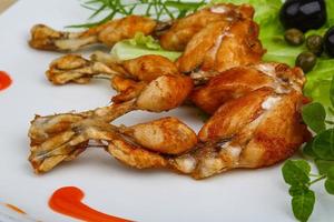 Fried frog legs on the plate and wooden background photo