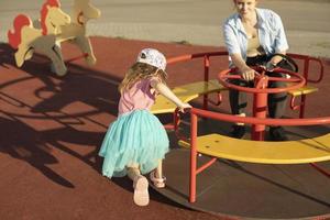 Child on carousel. Kids in playground. Girl spins swing. Details of game in summer. Bright frame game preschoolers. photo