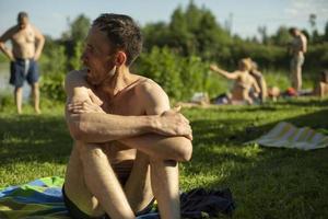 Guy sits on beach in summer. Man sunbathes in sun. Relax on hot day. photo