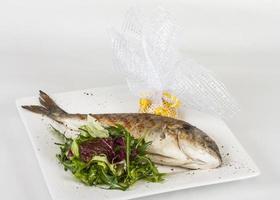 Dorada fish with salad on the white plate. Studio shot photo