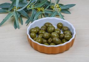 Green olives in a bowl on wooden background photo