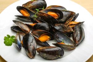 Boiled mussels on the plate and wooden background photo