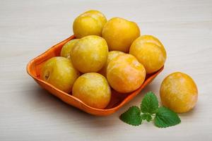 Yellow plums in a bowl on wooden background photo