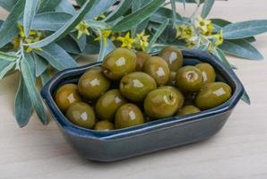 Green olives in a bowl on wooden background photo