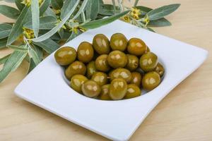 aceitunas verdes en un recipiente sobre fondo de madera foto