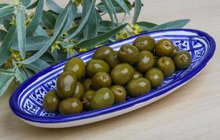 Green olives in a bowl on wooden background photo