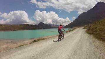 homme faisant du vélo sur un chemin de terre bordant un lac de montagne video