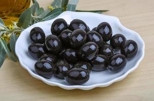 Black olives in a bowl on wooden background photo