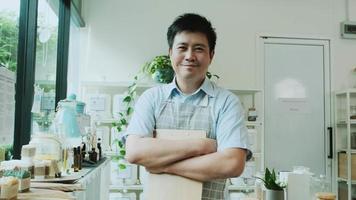 Portrait of Asian male shopkeeper smiles and looks at camera, arms crossed at refill store, natural products, zero-waste grocery, and plastic-free, eco environment-friendly, sustainable lifestyles.