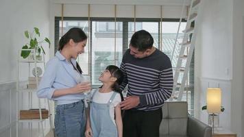 Happy healthy Thai family, little Asian girl stands and drinks fresh milk with young mum and dad in morning, smiles and joy together at lovely home, wellness nutrition, domestic breakfast lifestyle. video