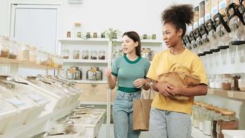 Two young female customers are choosing and shopping for organic products in refill store with reusable bags, zero-waste grocery, and plastic-free, texts BYO on wall means-bring your own container. video