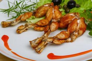 Fried frog legs on the plate and wooden background photo