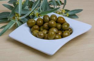 Green olives in a bowl on wooden background photo