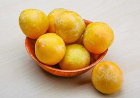 Yellow plums in a bowl on wooden background photo