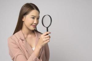 Young asian woman holding magnifying glass over white background, analysis and finance concept. photo