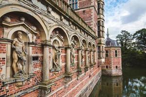 Antique sculptures near entrance to Frederiksborg castle in Copenhagen, Denmark - September, 24th, 2015. Red brick wall with statues reflected on the water of canal. photo