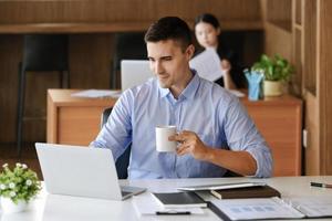 los gerentes de marketing masculinos toman café mientras trabajan para reducir la somnolencia antes de usar computadoras, ipads y documentos de análisis de marketing. foto