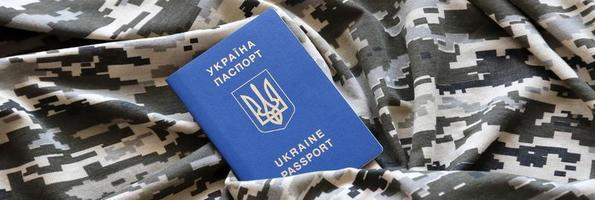 Ukrainian foreign passport on fabric with texture of military pixeled camouflage. Cloth with camo pattern in grey, brown and green pixel shapes and Ukrainian ID photo