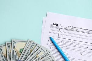 1065 tax form lies near hundred dollar bills and blue pen on a light blue background. US Return for parentship income photo