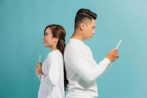 Distrust Concept. Beautiful young modern couple with smartphones in hands standing back to back. photo
