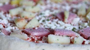 Frozen hawaiian pizza in low angle close-up view shows pineapple slices with ham and delicious herbs ready for fast food stove as homemade food for unhealthy eating with greasy cheese instant meal video