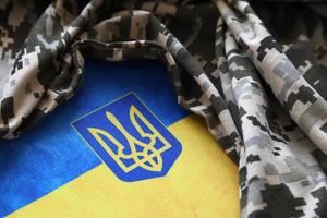 SUMY, UKRAINE - MARCH 20, 2022 Ukrainian flag and coat of arms with fabric with texture of pixeled camouflage. Cloth with camo pattern in grey, brown and green pixel shapes with Ukrainian trident sign photo