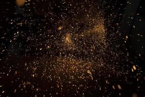 Sparks in dark. Lots of bright lights on black background. Burning metal particles fly in different directions. photo