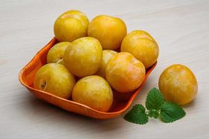 Yellow plums in a bowl on wooden background photo