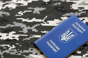 Ukrainian foreign passport on fabric with texture of military pixeled camouflage. Cloth with camo pattern in grey, brown and green pixel shapes and Ukrainian ID photo