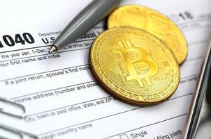 The pen, bitcoins and dollar bills is lies on the tax form 1040 U.S. Individual Income Tax Return. The time to pay taxes photo