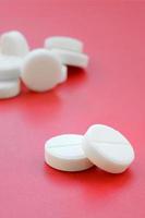 A few white tablets lie on a bright red background surface. Background image on medical and pharmaceutical topics photo