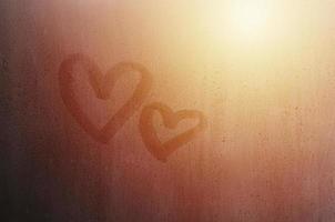 un par de símbolos de corazón de amor borrosos abstractos dibujados a mano en el cristal húmedo de la ventana con fondo de luz solar. plantilla para tarjetas postales del día de san valentín foto