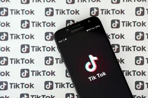 TERNOPIL, UKRAINE - MAY 2, 2022 Tik Tok smartphone app on screen and Many TikTok logo printed on paper. Tiktok or Douyin is a famous Chinese short-form video hosting service owned by ByteDance photo